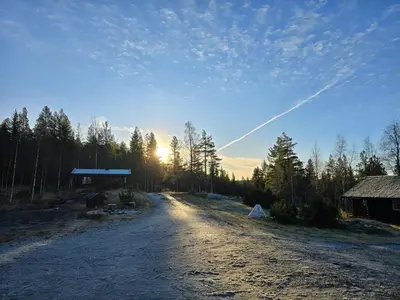 a dirt road with a barn and the sun in the sky at Smia cabin , A Unique Rustic Hideaway in Lii