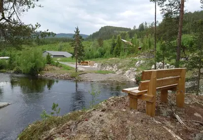 a wooden bench sitting next to a river at Smia cabin , A Unique Rustic Hideaway in Lii