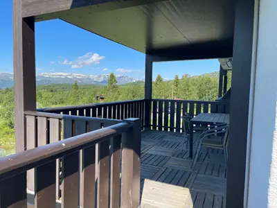 a deck with a table and chairs and mountains at 3-Roms Leilighet Nær Alle Beitostølens Fasiliteter in Beitostøl