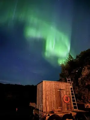 a wooden building with a ladder next to it under the aurora at Kuringen Brygge Hotel and Restaurant in Refsnes