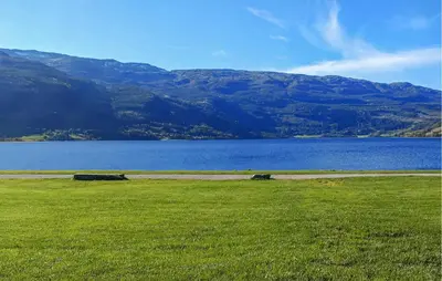 a field with a lake and mountains in the background at 3 Bedroom Beautiful Apartment In Voss in Vossevangen