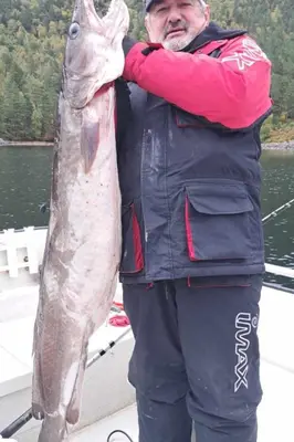 a man standing on a boat holding a large fish at Holiday Home Stabben Blue House by Interhome in Storsæter