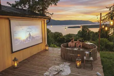 a man in a hot tub on a deck with a movie screen at Romantic Getaway Hot Tub, Cinema & View in Stange