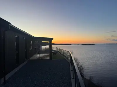 a house with a deck next to a body of water at Sunset Island Retreat, Brand New Waterfront Cabin in Herland