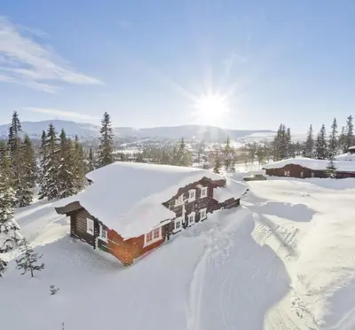 a house covered in snow with the sun behind it at Cabin at Fageråsen - 4 roomed family cabin for skiing in Trysil in Trysil