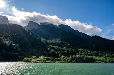 a view of a mountain from a lake with the sun at Central Stay Odda in Odda