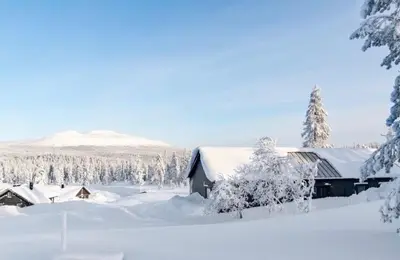 a house covered in snow with trees and mountains at Modern cabin with jacuzzi near Trysil alpine in Trysil