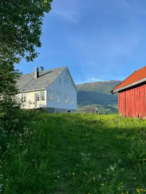 a blue house and a red barn in a field at Historic Timber House From The 1800S In Nordfjord in Olden