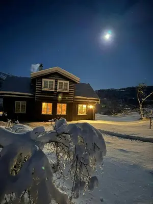 a house covered in snow at night with the moon at Elegant Mountain Cabin With Kjerringafjell View in Brekka