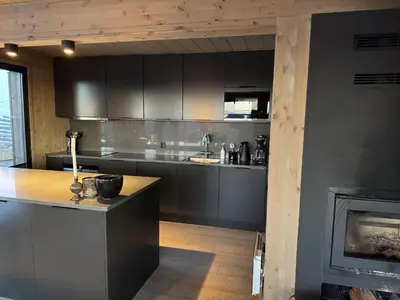 a kitchen with black cabinets and a fireplace at Beautiful Ski-in Ski-out Cabin at the top of the mountain in Hafjell in Hafjell