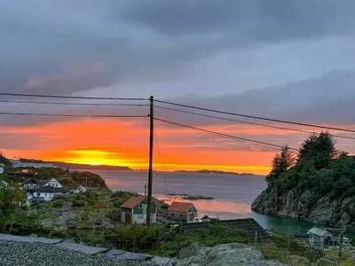 a sunset over the ocean with houses on a cliff at Cabin On Hilltop With Beach And Sea Views in Bekkjarvik