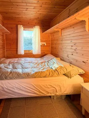 a bed in a log cabin with a window at Cabin On Hilltop With Beach And Sea Views in Bekkjarvik