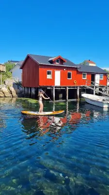 a woman on a surfboard in the water near a house at Mausund- Øyperla i havet! Egen båtplass ved hytta! in Frøya