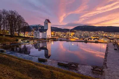 a church with a reflection in the water at sunset at Cozy loft apartment in the heart of Bergen in Bergen