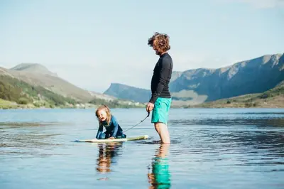 a man and a little girl on a surfboard in the water at Large house with Ocean view at Ervik and Vestkapp