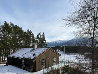 a small house in the snow with mountains in the background at Bosdalhuset in Lavik