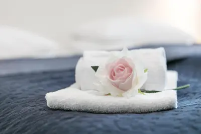 a white towel with a pink rose on a bed at Kinn Hotell Florø in Florø