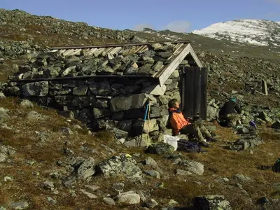 a person sitting in front of a small stone building at Strind Gard, Visdalssetra in Boverdalen
