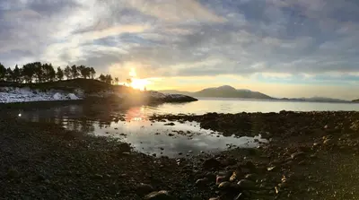a sunset on the shore of a body of water at Tustna Ladestasjon in Hals