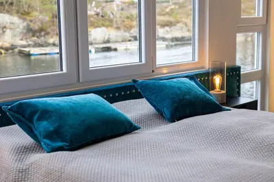 a bed with two blue pillows in a room with windows at Floating Villa Bergen in Bergen
