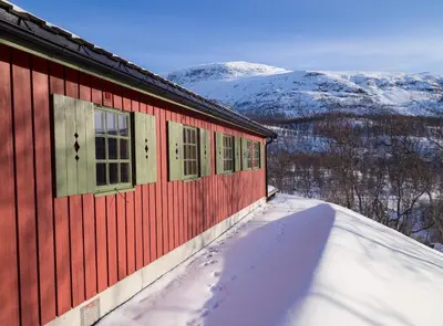 a red building in the snow with mountains in the background at Maristuen Fjellferie in Borgund