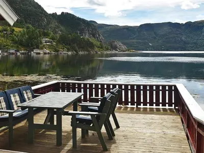 a wooden deck with a table and chairs next to a lake at 8 person holiday home in Sundlandet in Snildal
