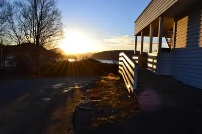a sun setting behind a house with a fence at VIKEDAL VERTSHUS hotel in Vikedal