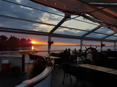 people sitting at tables on a deck watching the sunset at Idylliske Evjua ved Mjøsa in Skreia