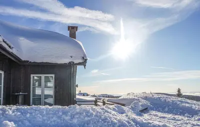 a house covered in snow with the sun behind it at Cozy Home In Sjusjøen With Sauna in Sjusjøen