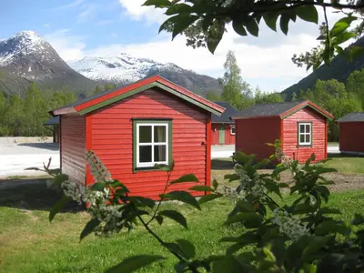 a small red house with mountains in the background at Jostedal Camping in Jostedal