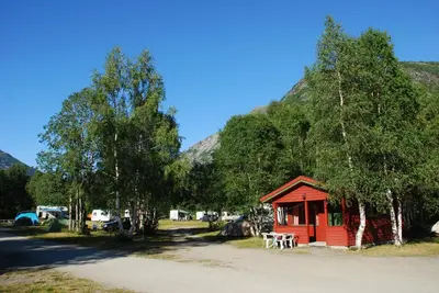 a small red cabin with trees and mountains in the background at Jostedal Camping in Jostedal