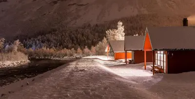 a building with snow on the ground next to a river at Jostedal Camping in Jostedal