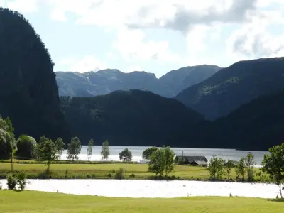 a field with a lake and mountains in the background at Rongen gard in Bolstadøyri
