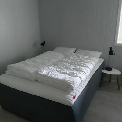 an unmade bed in a bedroom with a lamp on a table at Mørkve Apartement in Myrkdalen