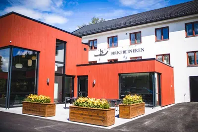 a red and white building with some plants in boxes at Birkebeineren Hotel & Apartments in Lillehammer