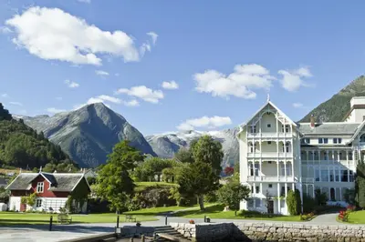 a large white house with mountains in the background at Kviknes Hotel in Balestrand