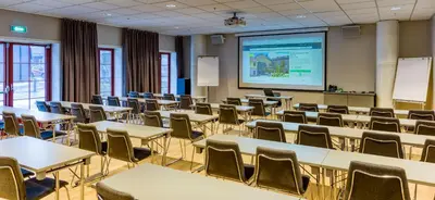 an empty classroom with tables and chairs and a projection screen at Home Hotel Hammer in Lillehammer