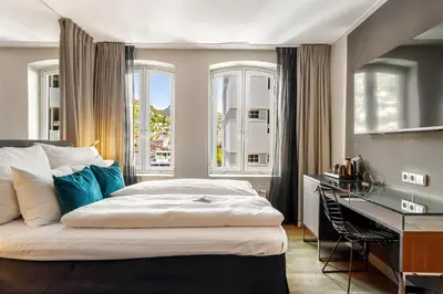 a bedroom with a bed and a desk and windows at Clarion Hotel Admiral in Bergen