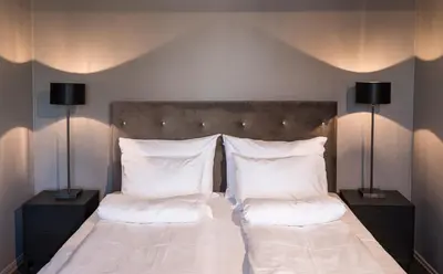 a bedroom with a bed with white pillows and two lamps at Klækken Hotel in Hønefoss