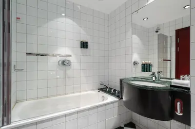 a white tiled bathroom with a tub and a sink at Home Hotel Bryggen in Bergen