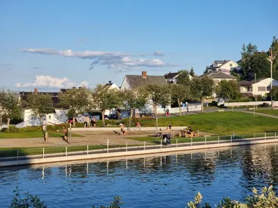 a group of people sitting on the grass by the water at Gjøvik Hovdetun Hostel in Gjøvik