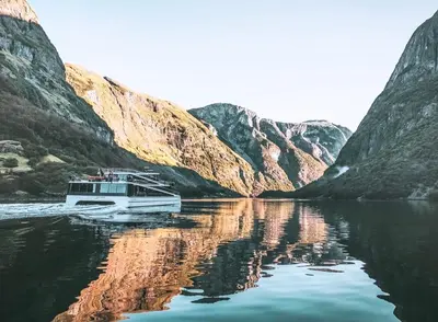 a boat on a river between two mountains at Gudvangen Fjordtell in Gudvangen
