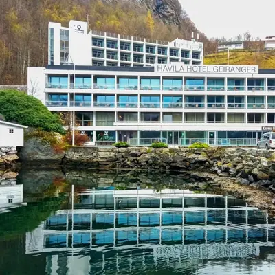 an office building with a reflection in a body of water at Havila Hotel Geiranger in Geiranger