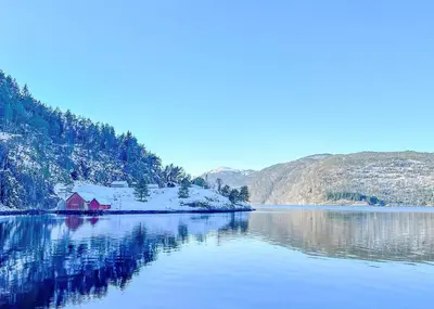 a lake with a red house and snow covered mountains at Ryfylke Fjordhotel in Sand