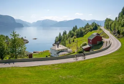 two people riding bikes on a road next to a lake at Lavik Fjord Hotel & Apartments in Lavik