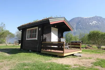 a small black cabin with a porch and a mountain at Trollstigen Resort in Åndalsnes