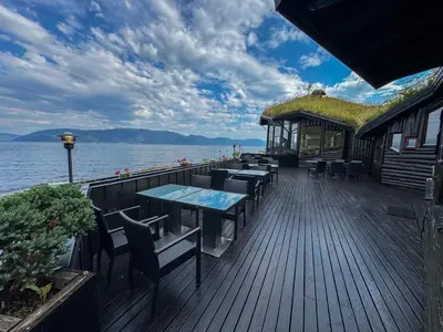 a wooden deck with tables and chairs on the water at Brekkestranda Fjordhotel in Brekke