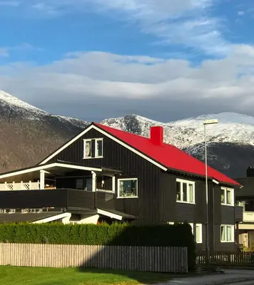 a black house with a red roof with mountains in the background at Villa Åndalsnes in Åndalsnes