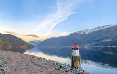 a lighthouse on the shore of a lake with mountains at 2 Bedroom Cozy Home In Vallavik in Vangsbygd