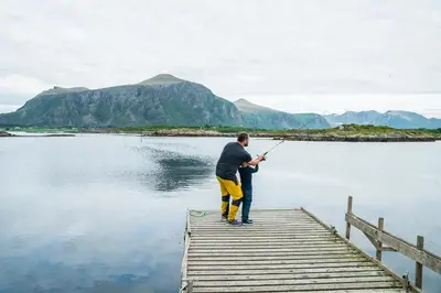 a man standing on a dock fishing on a lake at Hustadvika Havhotell - by Classic Norway Hotels in Farstad
